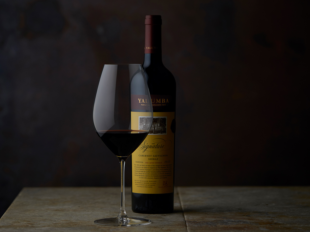 The Signature wine bottle and filled glass on wooden surface