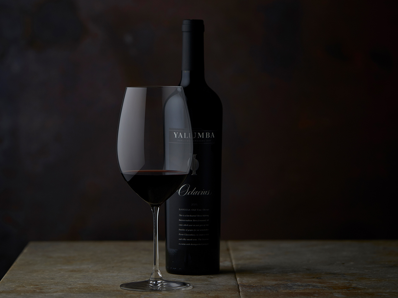 The Octavius wine bottle and filled wine glass on wooden surface